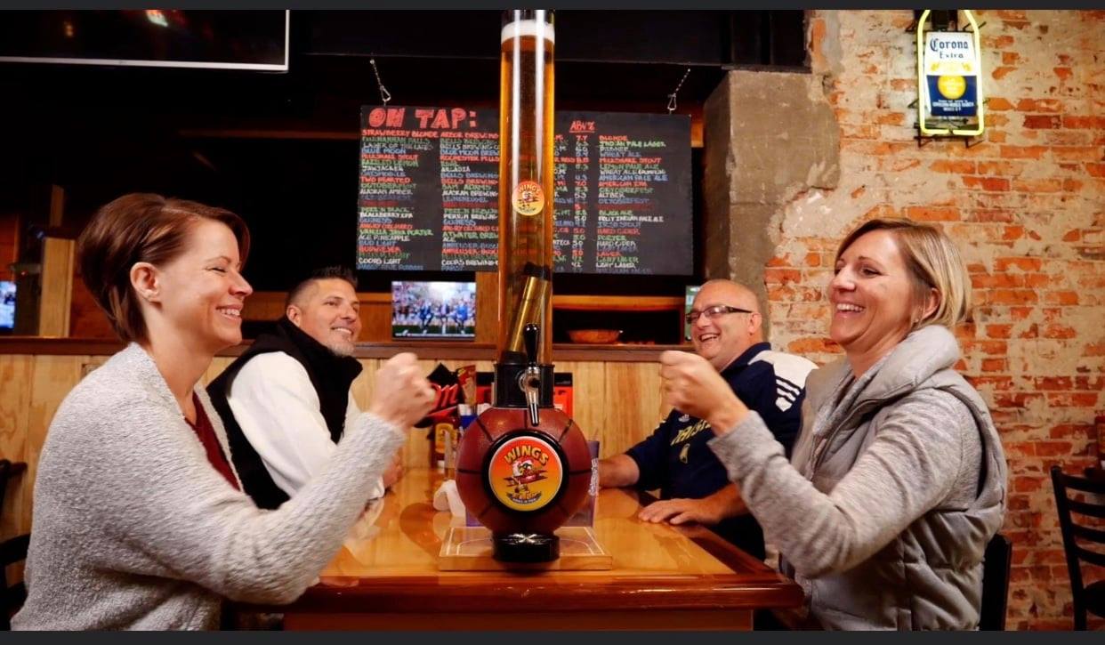 people sitting at a table with a 100 ounce beer tube dispenser with a basketball themed base.