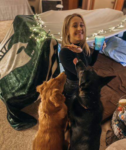 a girl and two dogs next to a blanket fort