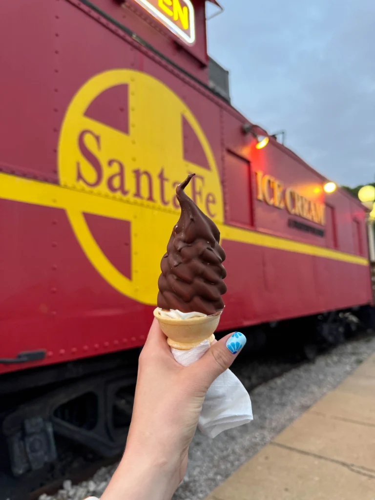 Vanilla Ice cream cone with chocolate dip held up outside the Whistle Stop Ice cream caboose