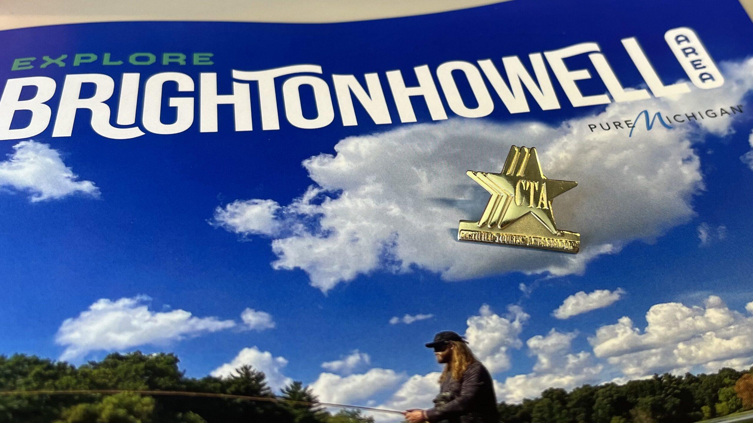 Explore Brighton Howell Area in big white letters, bright blue sky on cover of magazine with gold star pin sitting on top.