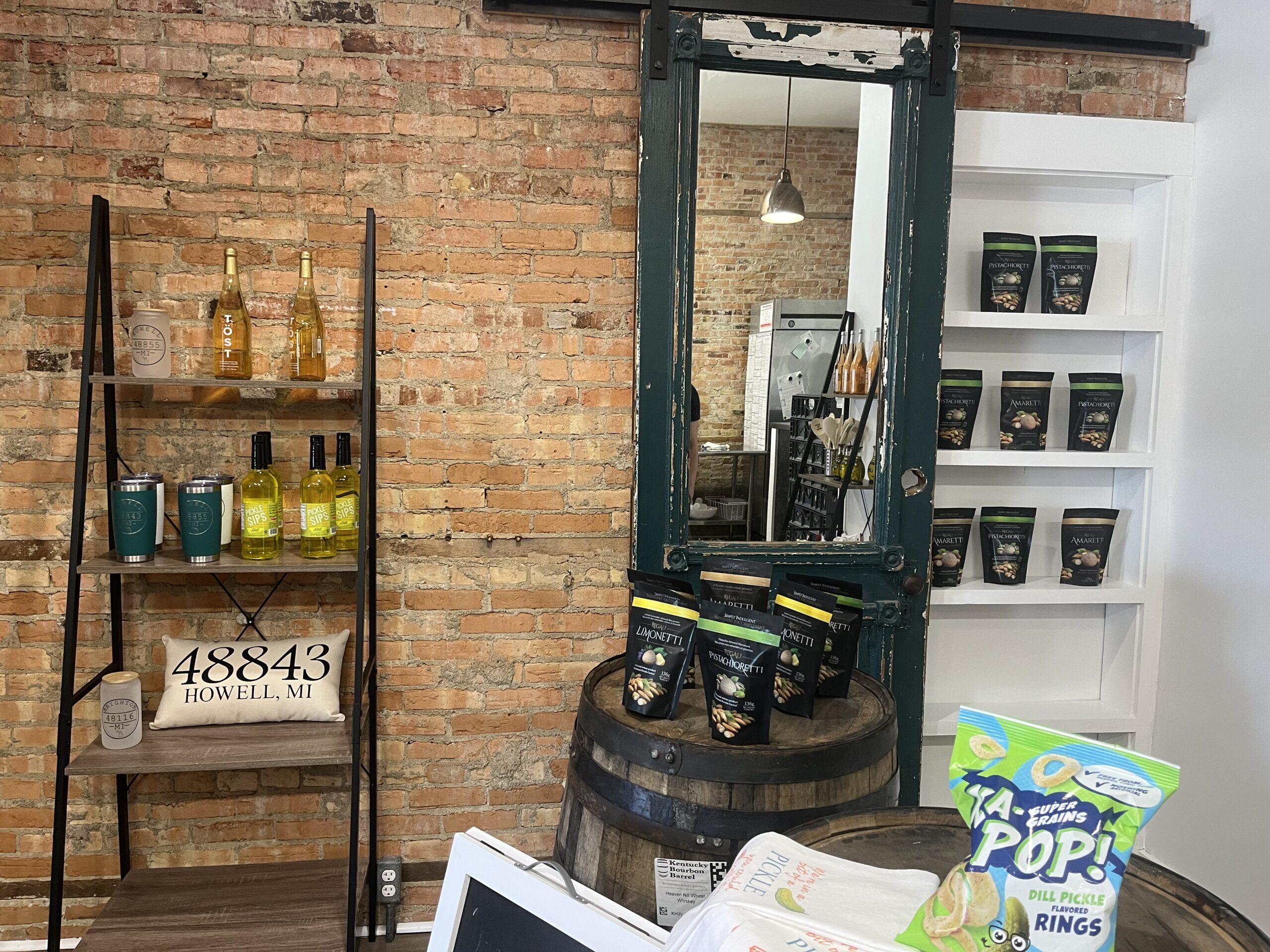 Sales racks at crunchy pickle. Shelves against brick wall with bottles and bags of pistachios and oils. Mirror in view.