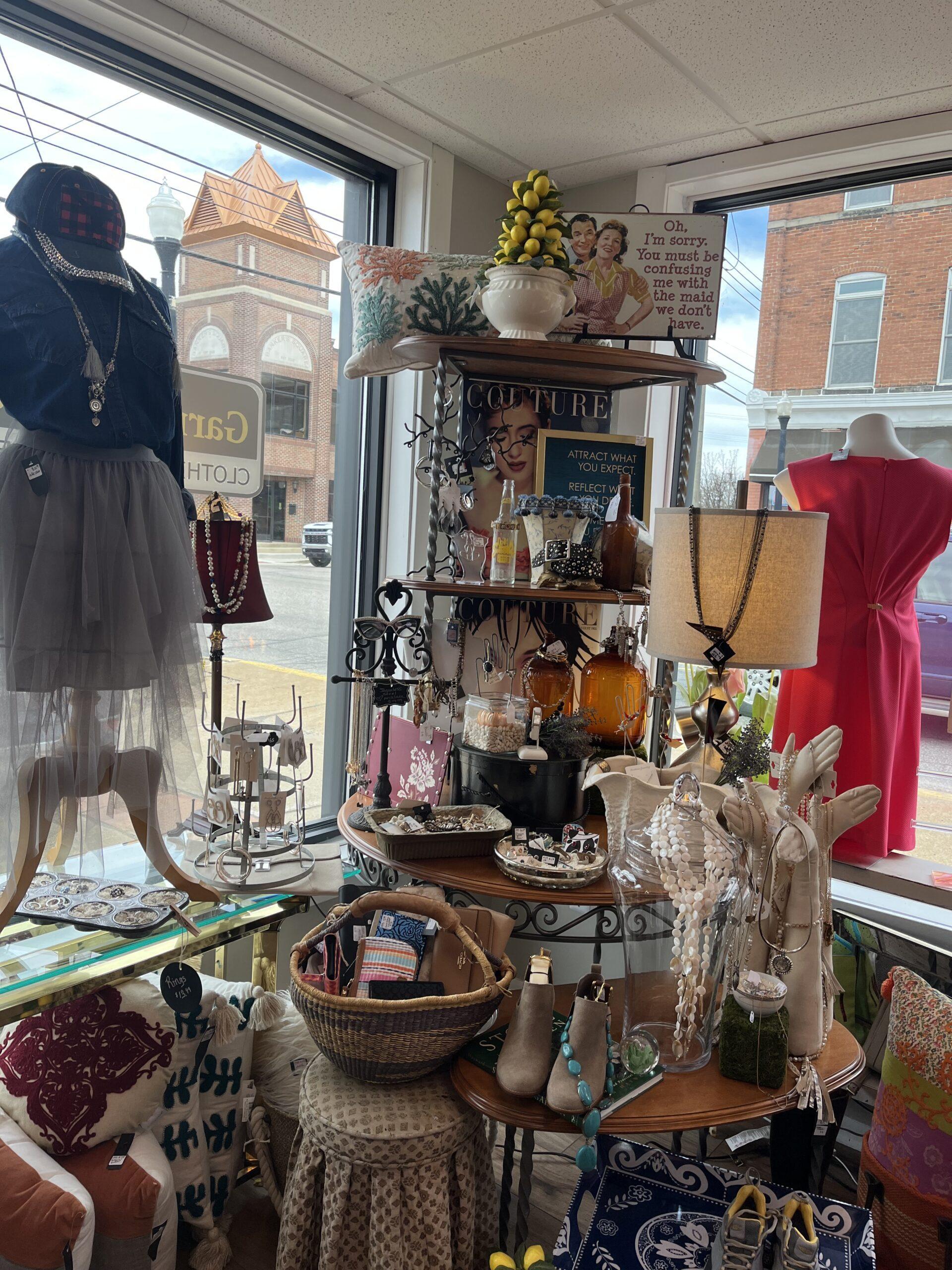 Clothes, jewlery, and other items on display at corner of store with windows behind.
