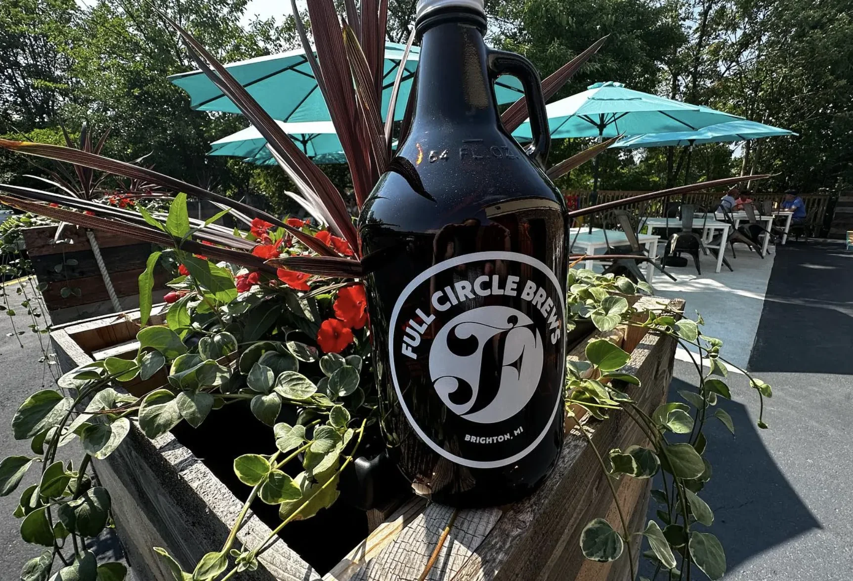 A bottle labeled with Four Circle Brewery's logo next to a flower bush.
