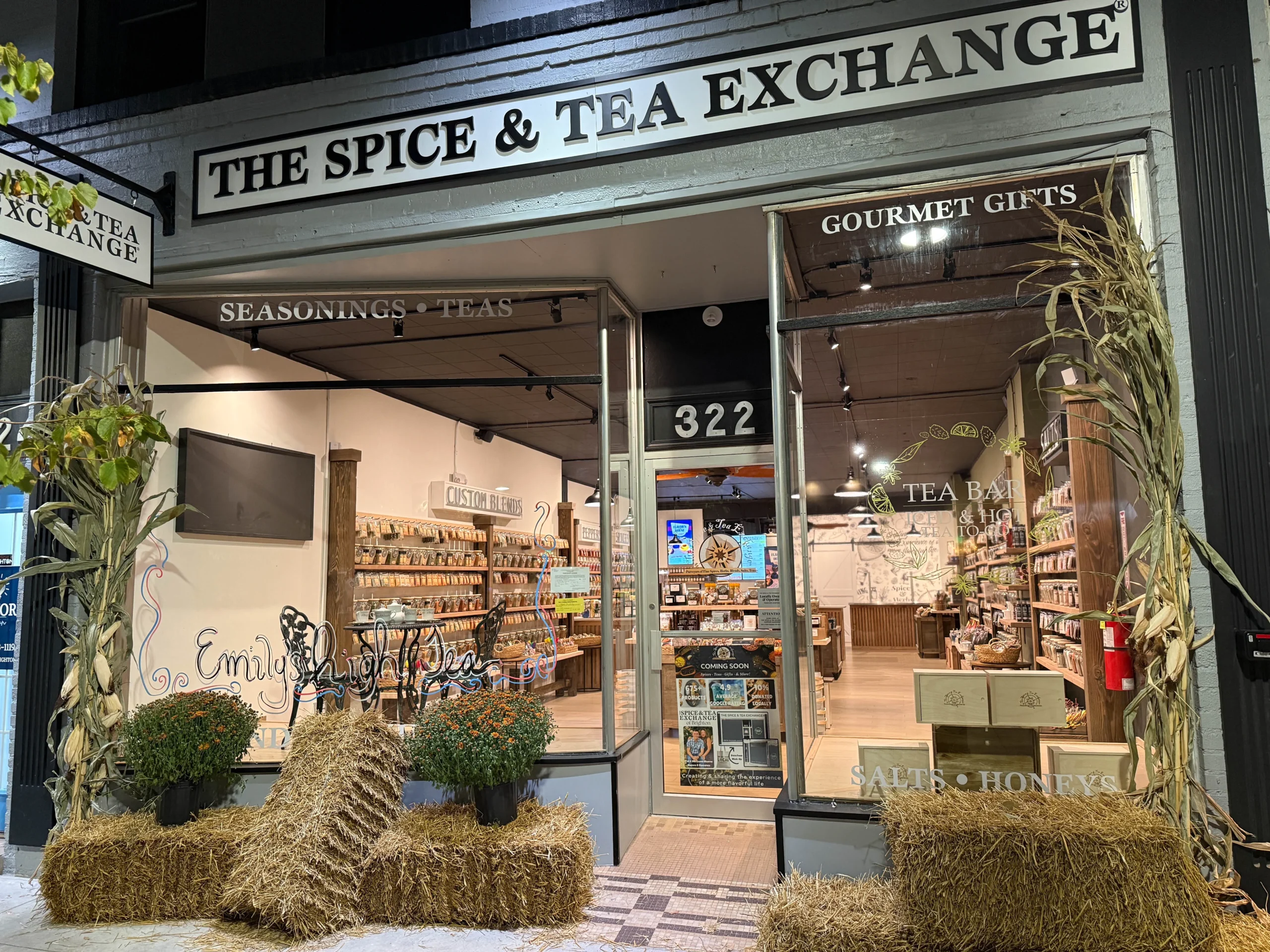 The Spice & Tea Exchange of Brighton storefront with fall decor in downtown at night.